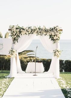 an outdoor ceremony setup with white flowers and greenery on the grass near the ocean