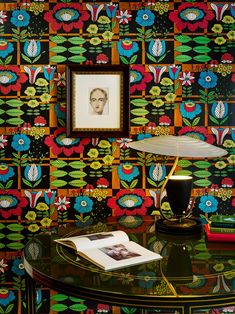 a table with a lamp and a book on it in front of a colorful wallpaper