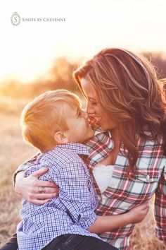 a woman holding a small child and kissing her face with the sun setting in the background