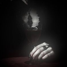 a woman's hand holding onto a wine glass in the dark with her nails on it