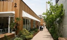 people are walking down the sidewalk in front of a building with wooden walls and white awnings