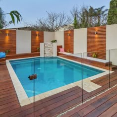 an empty swimming pool surrounded by wooden decking and fenced in area with lights