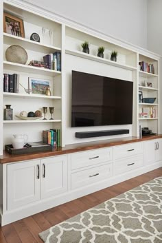 a large flat screen tv sitting on top of a white bookcase in a living room