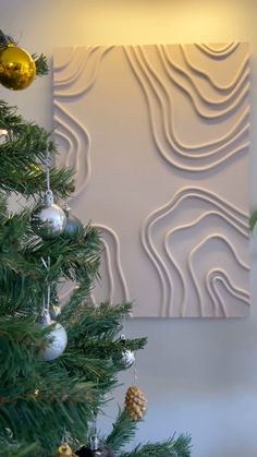 a christmas tree in front of a white wall with ornaments hanging from it's branches