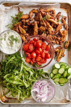 a tray filled with chicken wings, tomatoes, cucumbers and lettuce