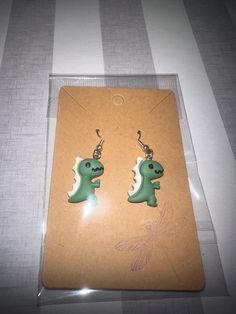 the earrings are green and white with a small dinosaur on it's earwires