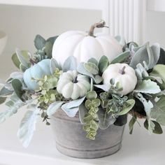 a potted plant with white pumpkins and greenery in it on a table