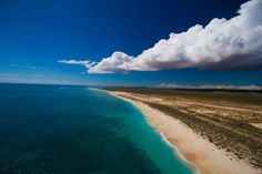 an aerial view of the beach and ocean with clouds in the blue sky above it