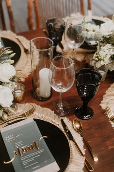 the table is set with black and gold place settings, silverware, and white flowers