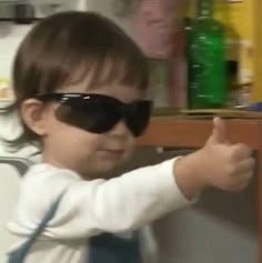 a young child wearing sunglasses and holding something in his hand while standing next to a refrigerator