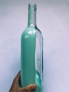 a hand holding a green glass bottle in front of a white wall with the bottom half open