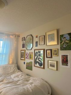 a bed sitting under a window next to a wall covered in pictures and framed art