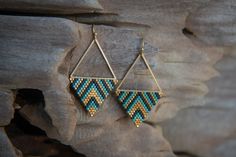 a pair of gold and blue beaded earrings hanging from a piece of driftwood