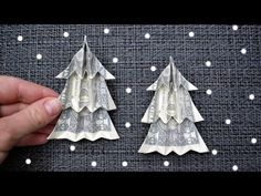 two origami christmas trees made out of dollar bills are being held by someone's hand