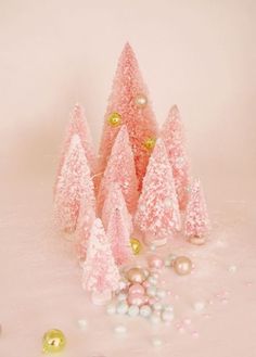 pink christmas trees with gold ornaments and pearls on the ground in front of them, against a white background