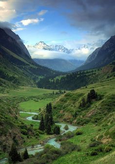 the mountains are covered in clouds and green grass, with a river running through them