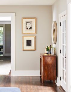 two framed pictures hang on the wall above a wooden cabinet in a room with hardwood floors