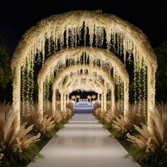 an outdoor walkway decorated with white flowers and greenery for a wedding ceremony at night