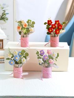 three small vases with flowers in them on a white table next to a blue chair