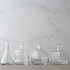 three clear glass bottles sitting on top of a white table next to a marble wall