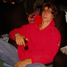 a man in a red hoodie sitting on a couch with a bottle of beer