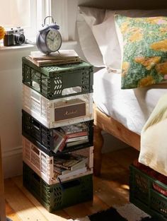 a stack of books sitting on top of a wooden floor next to a bed in a bedroom