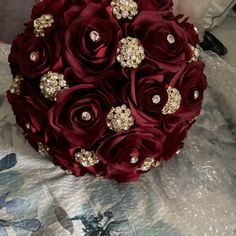 the bridal bouquet is made up of red roses and gold jeweled brooches