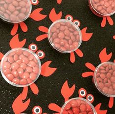 several plastic containers filled with candy sitting on top of a black table covered in red crabs