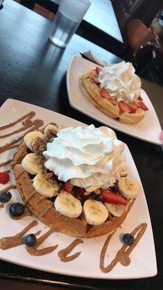 two waffles topped with whipped cream and fruit on a white plate next to each other