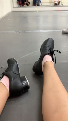 a person wearing black shoes and pink socks sitting on the floor with their legs crossed