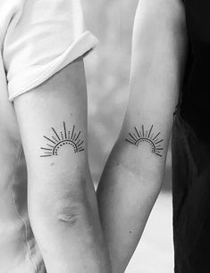 two people holding hands with tattoos on their arms and one has the sun behind them