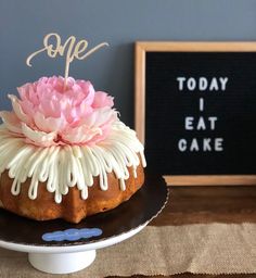 a cake sitting on top of a black plate with white icing and a pink flower