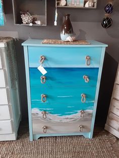 a blue chest of drawers with rope handles and sea scene painted on the front side