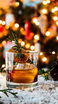 a glass filled with an alcoholic drink on top of a table next to a christmas tree