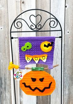 a crocheted halloween decoration hanging from a metal rack on a wooden fence with white boards in the background