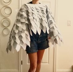 a woman standing in front of a door wearing a white and grey ponched cape