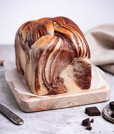 a loaf of bread sitting on top of a wooden cutting board next to chocolate pieces