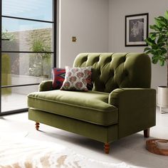 a green couch sitting in front of a window next to a rug and potted plant