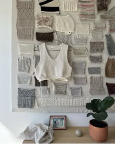 there are many knitted sweaters hanging on the wall next to a potted plant