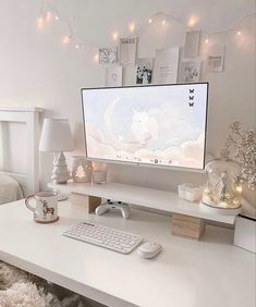 a white desk with a computer monitor and keyboard on it, surrounded by christmas lights