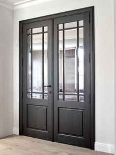 an empty room with two black doors and wood flooring, in front of a white wall