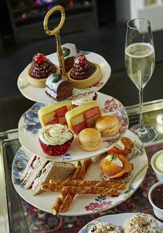 three tiered trays filled with different types of desserts and pastries next to two glasses of wine