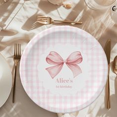 a pink and white plate with a bow on it sitting next to silverware, forks and spoons