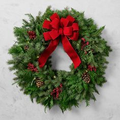 a christmas wreath with red ribbon and pine cones on a marble surface, top view