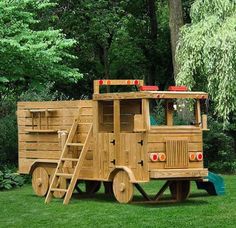 a wooden truck with ladders parked on the grass in front of trees and bushes