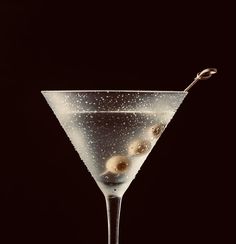 a martini glass filled with liquid and topped with three olives on a black background