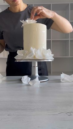 a woman is decorating a cake with white icing and tissue paper on the table