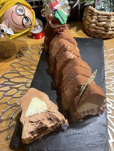 a piece of chocolate cake on a black plate with a doll in the back ground