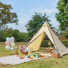 a tent set up in the grass with balloons and picnic food on it for an outdoor party