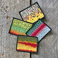 three colorful coasters sitting on top of a wooden table with dots and lines painted on them